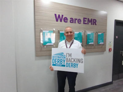 Will Rodgers holding an 'I'm backing Derby' sign in front of a 'We are EMR' sign