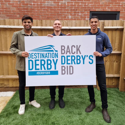 Young rail professionals holding a 'Back Derby's bid' sign